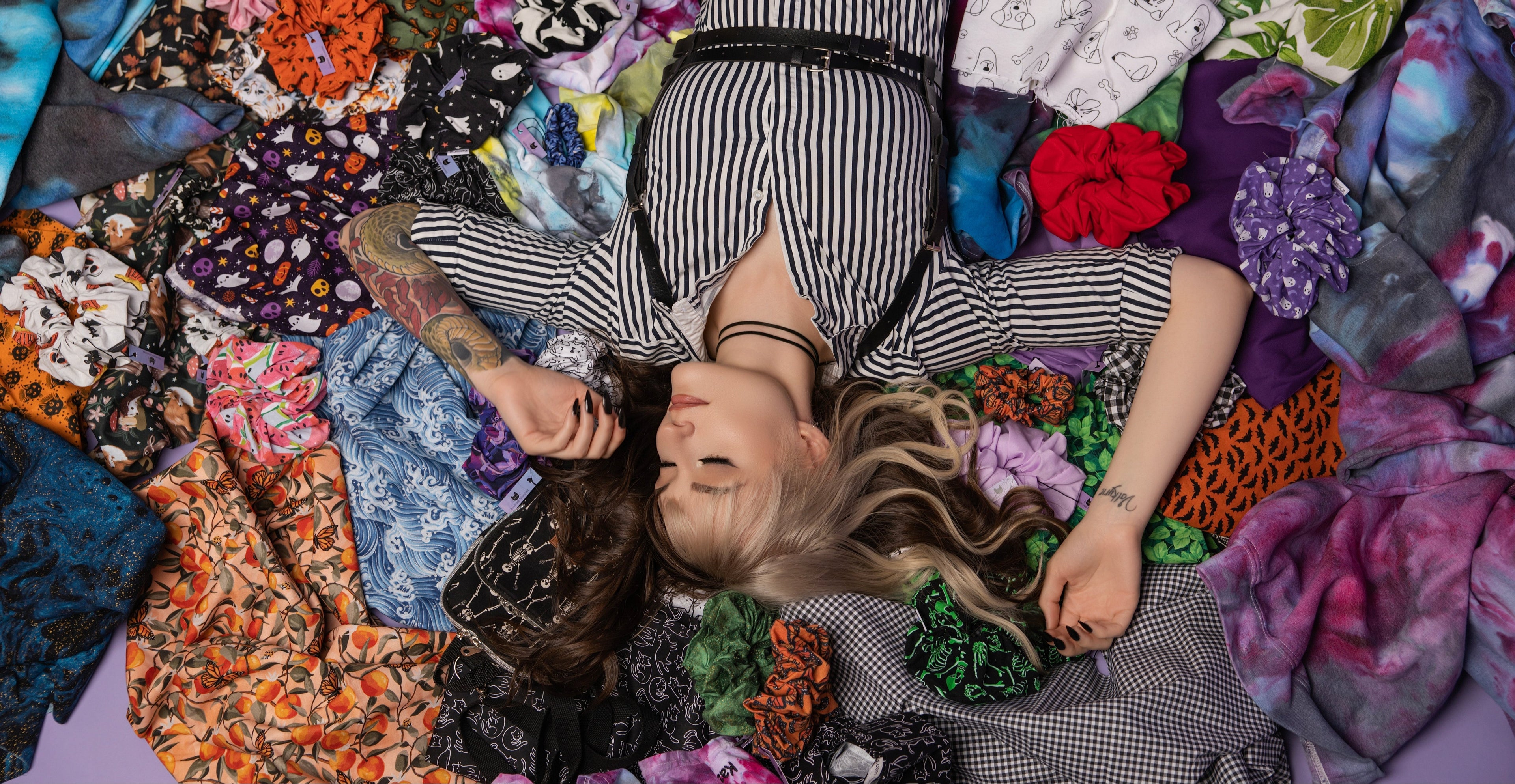Person lying on a bed of colorful fabric swatches with a purple background