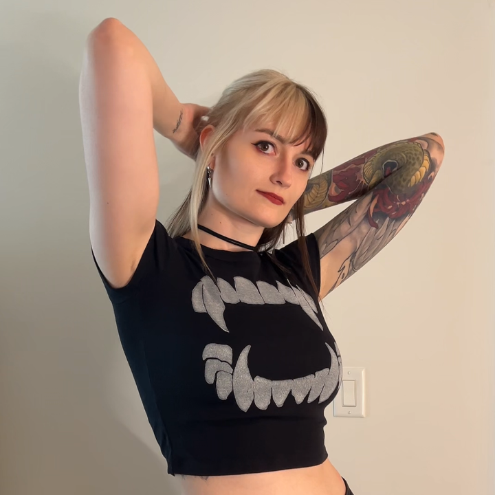 Person wearing a black crop top with a graphic design and black pants against a plain background