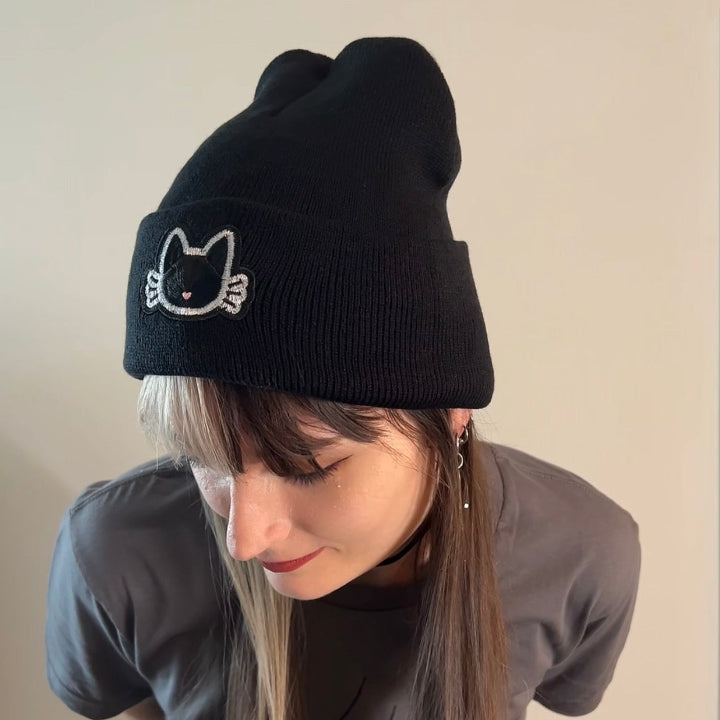 Person wearing a black beanie with a cat design on a beige background
