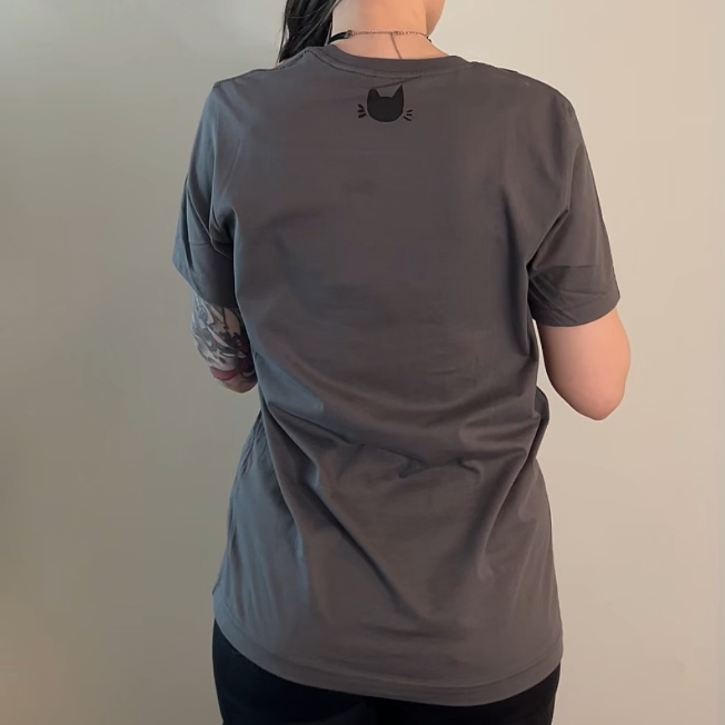 Person wearing a gray t-shirt with a black cat logo on the back against a plain background