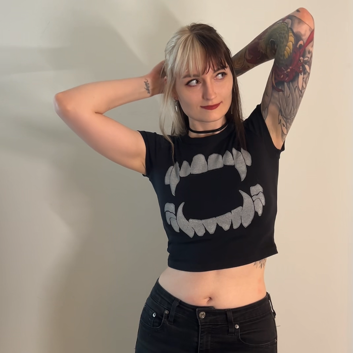 Person wearing a black crop top with a graphic design and black pants against a plain background