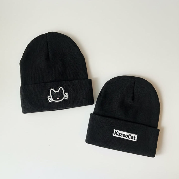 Two black beanies with cat logos on a white surface.