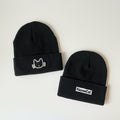 Two black beanies with cat logos on a white surface.