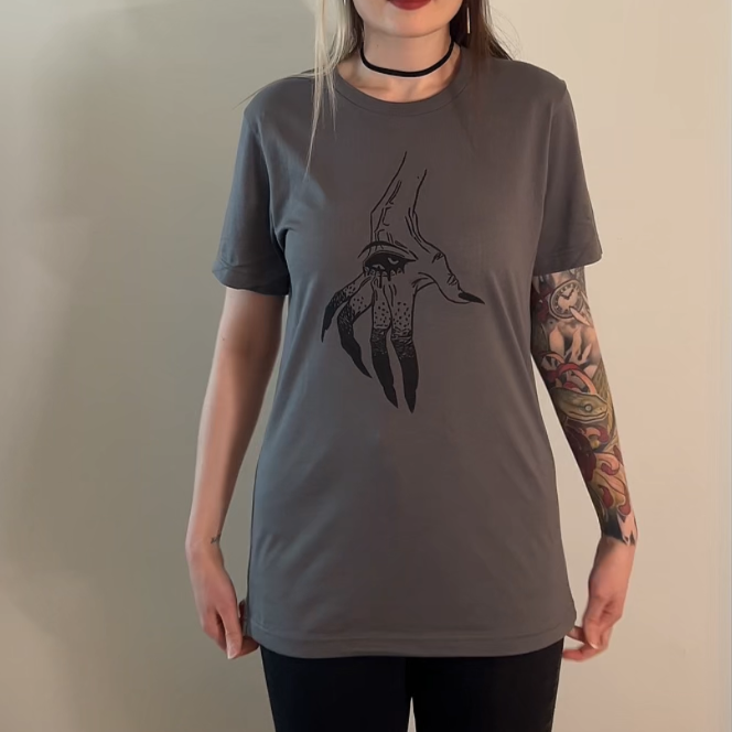 Person wearing a gray t-shirt with a graphic design on a plain background