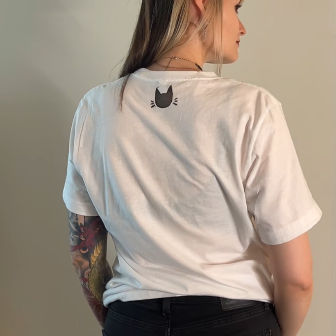 Person wearing a white t-shirt with a graphic design, standing against a plain wall.