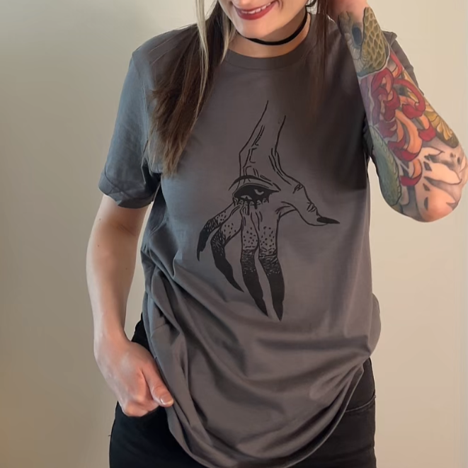 Person wearing a gray t-shirt with a graphic design, standing against a plain wall.