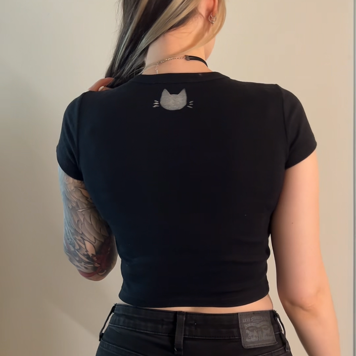 Person wearing a black t-shirt with a small graphic on the back against a plain background