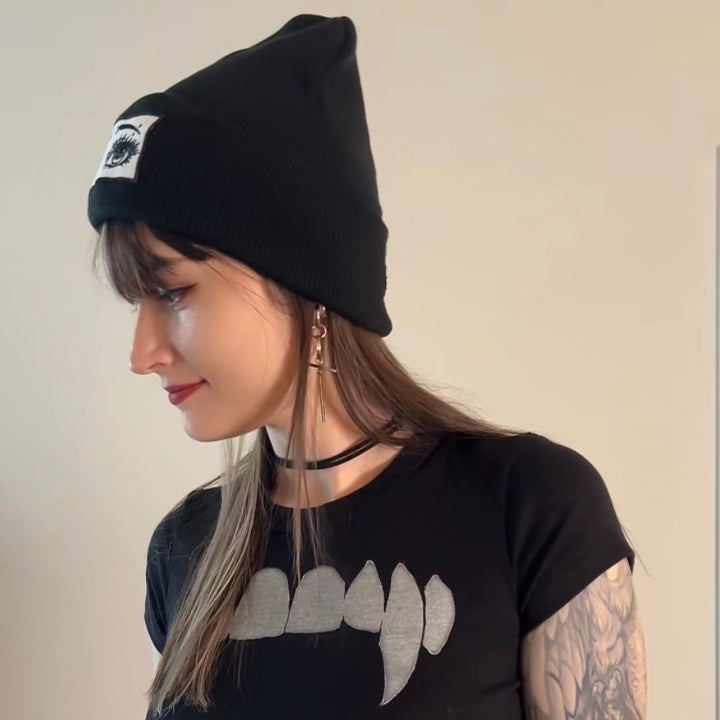 Person wearing a black crop top with a graphic design and a black beanie.