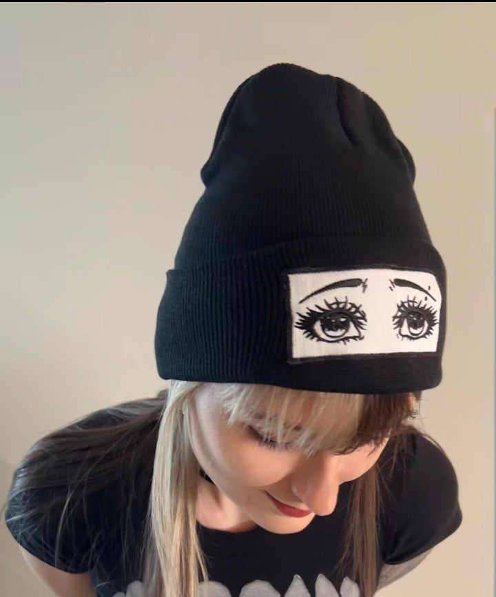 Person wearing a black beanie with eye design on a plain background
